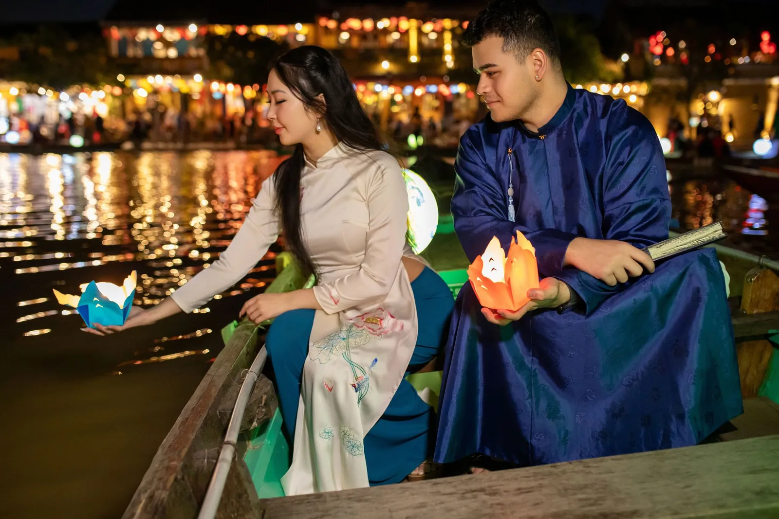 Honeymoon in Vietnam: a couple in traditional ao dai releasing paper lanterns from a boat on the Thu Bon River in Hoi An at night